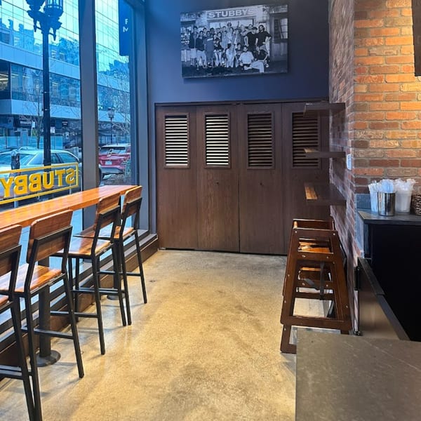Interior of Stubbys restaurant with bar seating, brick wall, and a large window looking out onto a city street.