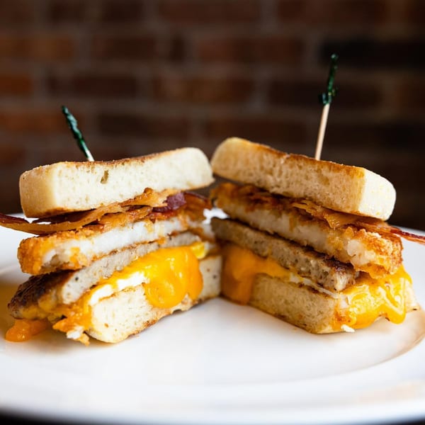 Two halves of a breakfast sandwich with melted cheese, bacon, and sausage on toasted bread.