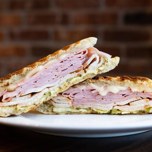Stubbys' American panini sandwich, cut in half, revealing layers of meat, cheese, and pickles.
