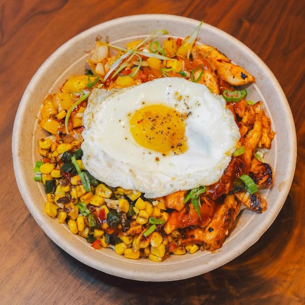 Stubbys' chicken bowl with corn, peppers, and a fried egg, on a wooden table.