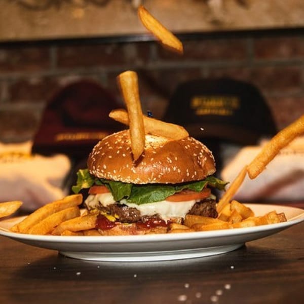 A Stubbys burger with melted cheese, lettuce, and tomato, surrounded by fries, with some fries floating.